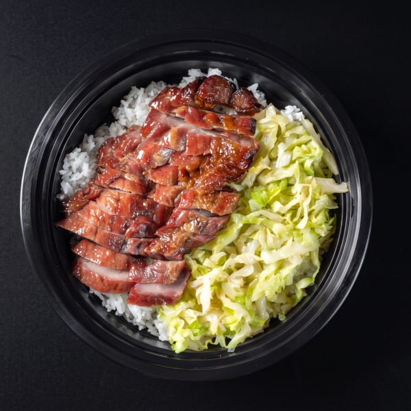 Overhead view of a black bowl with white rice, sliced char siu, and green cabbage.