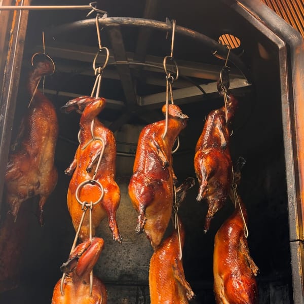 Several whole roasted ducks with crispy, golden-brown skin hang inside a dark oven.