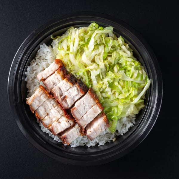 Top-down view of a takeout bowl with white rice, crispy pork belly, and shredded cabbage.