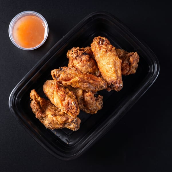 Crispy fried chicken wings in a black takeout container with a side of dipping sauce.