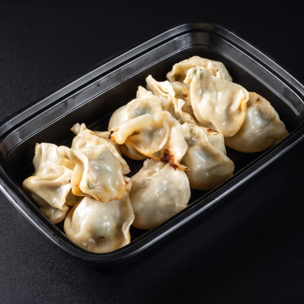 Pan-fried dumplings with crispy bottoms in a black takeout container on a dark surface.